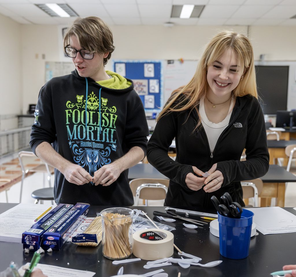 two teens laughing over a classroom project.
