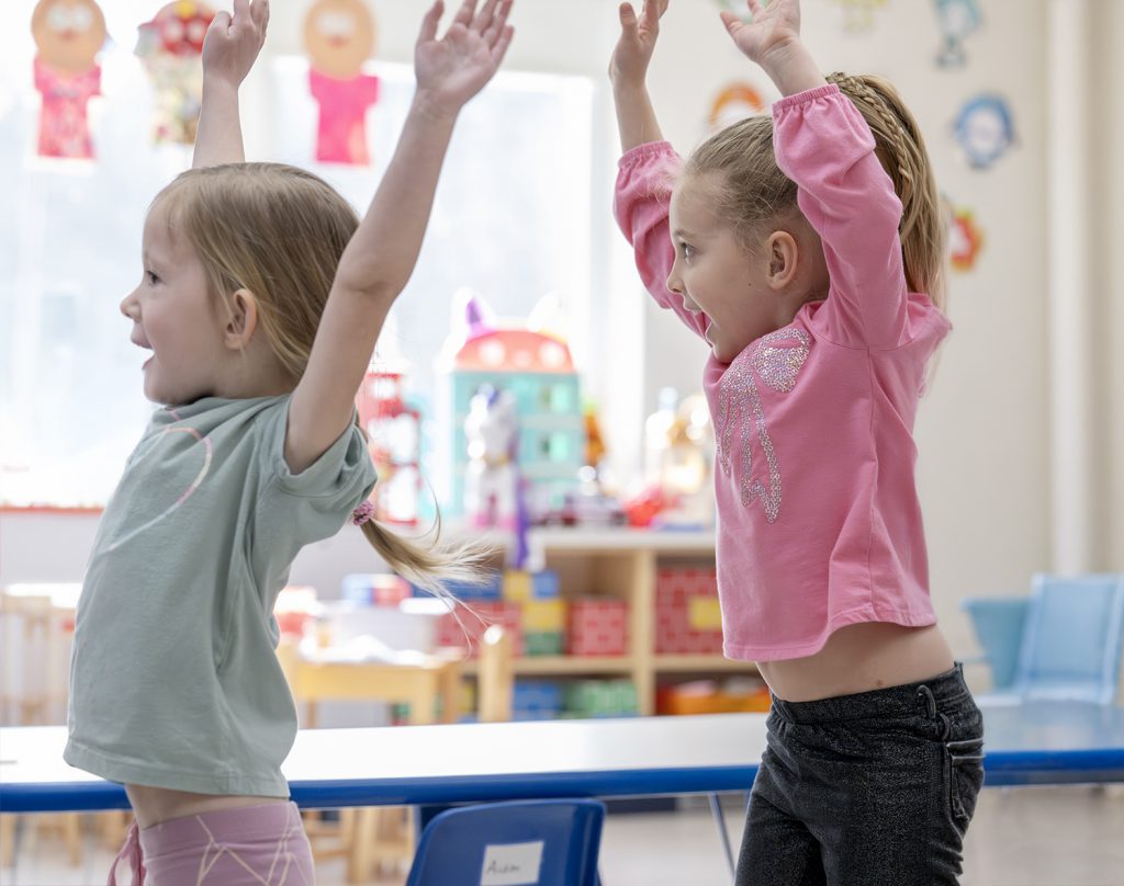 two young children jumping in the classroom.