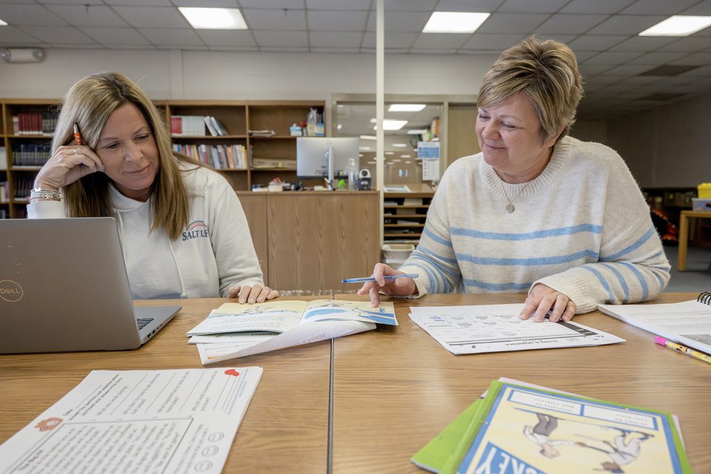 two teachers preparing lesson plans in a library setting.