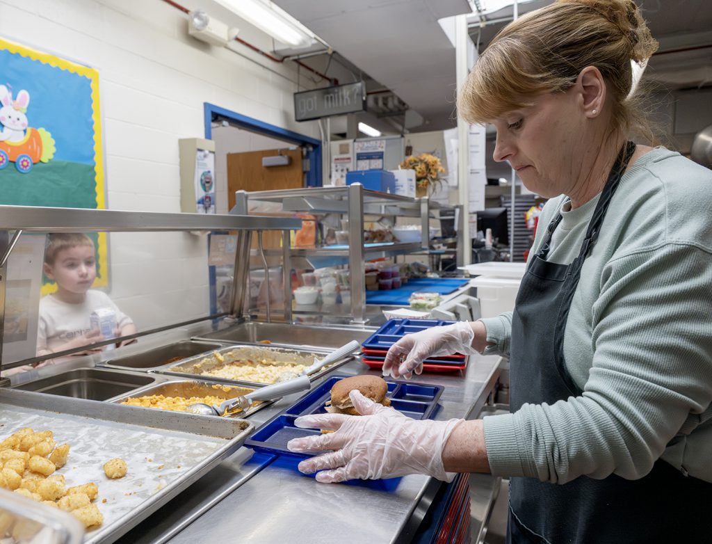 a food service worker preparing a lunch tray for a young student.