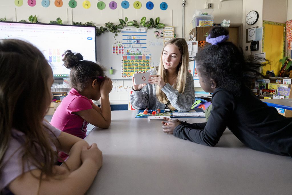 a young teacher displays flash cards to children in a classroom setting.