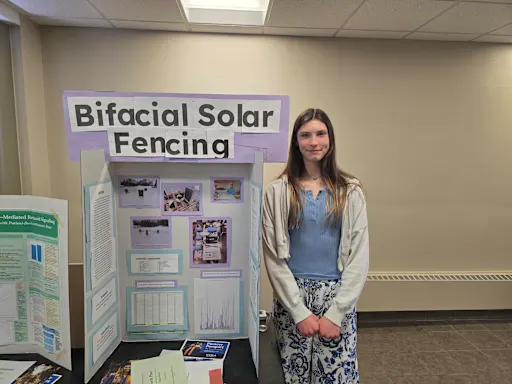 student standing next to their project, 'bifacial solar fencing', at the utica university science fair