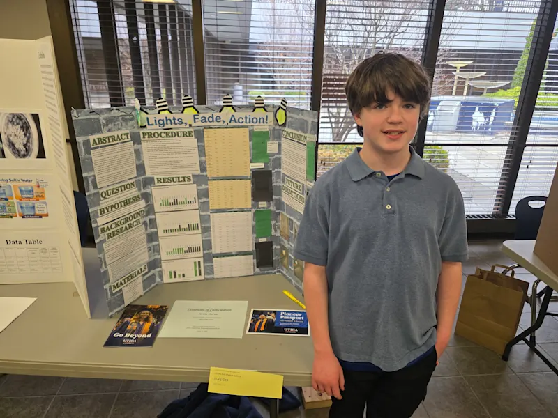 young student standing next to their project, 'lights fade action', at the utica university science fair