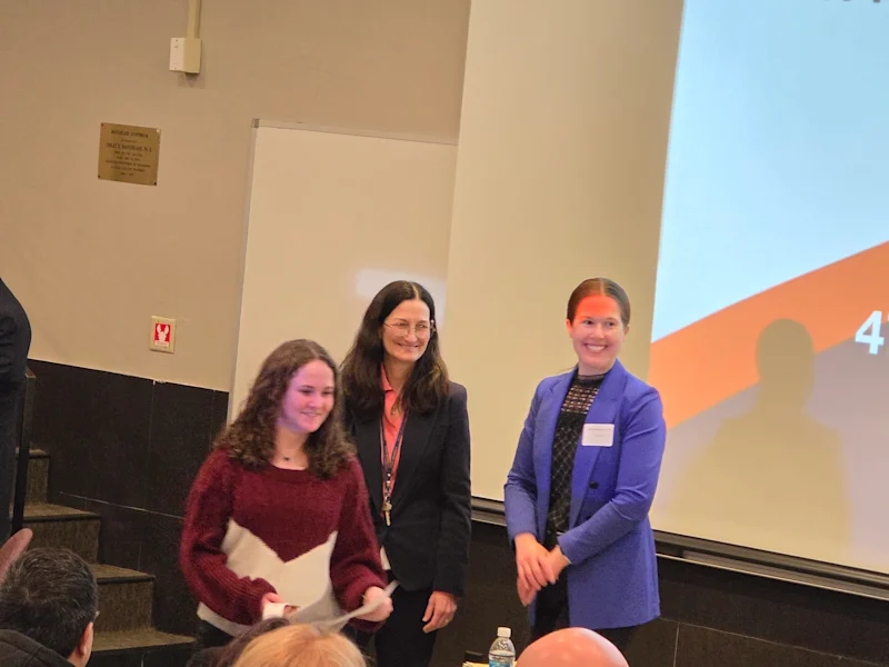 smiling student receiving a certificate at the utica university science fair, standing posing with two others who gave the award