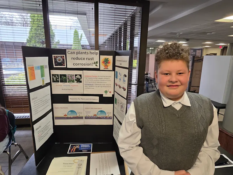 young student standing with their science project, 'can plants help reduce rust corrosion', at the utica university science fair