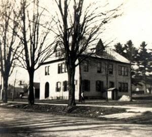 a two story building flanked by mature trees.