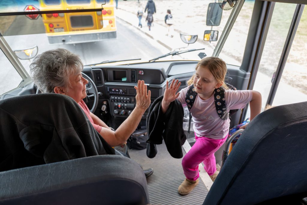 Bus driver giving student high five inside bus