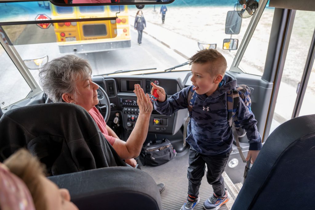 Student high fiving bus driver inside bus