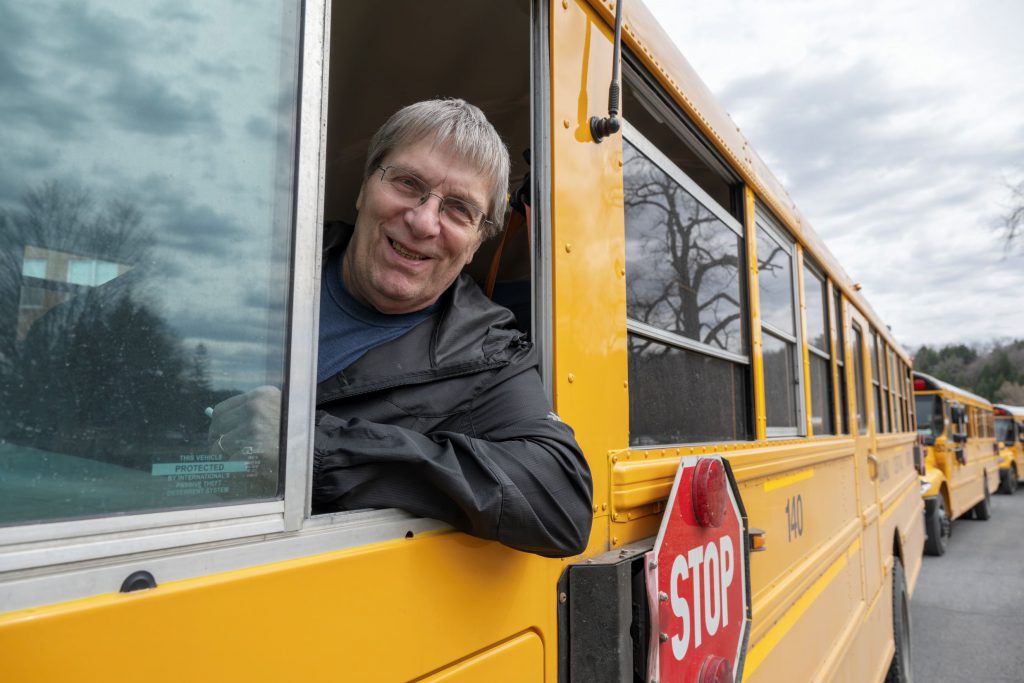 Bus driver smiling on driver side out window.