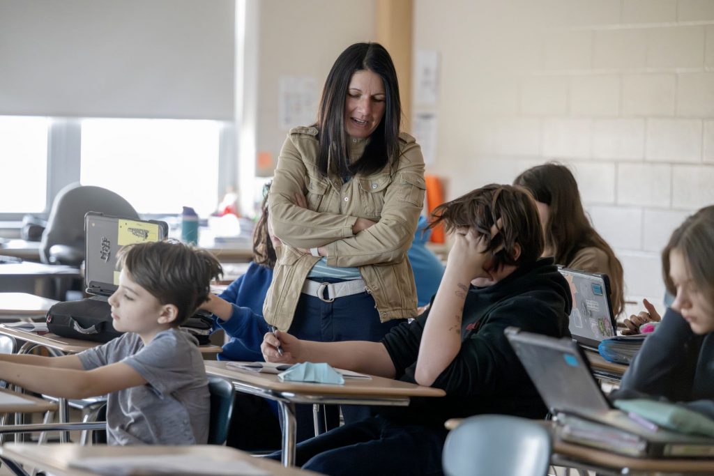 teacher standing over student chatting with them.