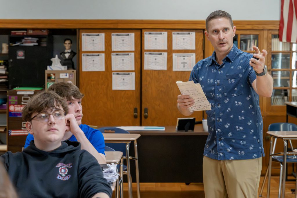 Teacher with paper in hand directing student's attention.
