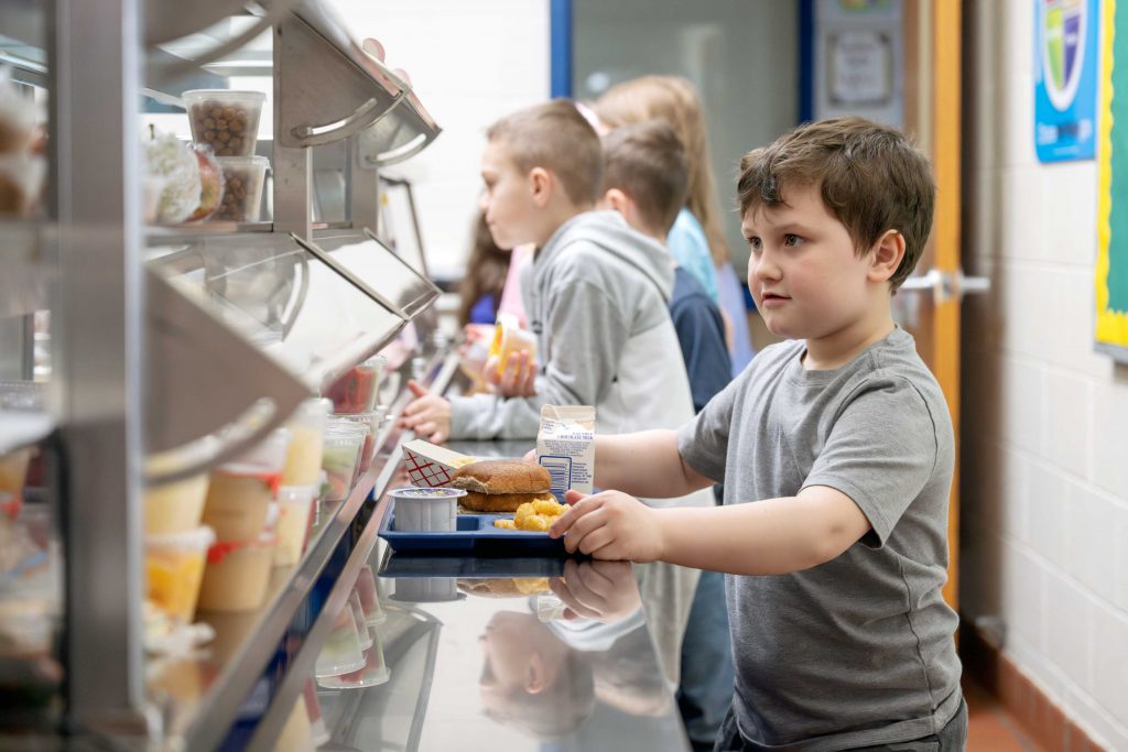 Child in line holding lunch in lunch tray.