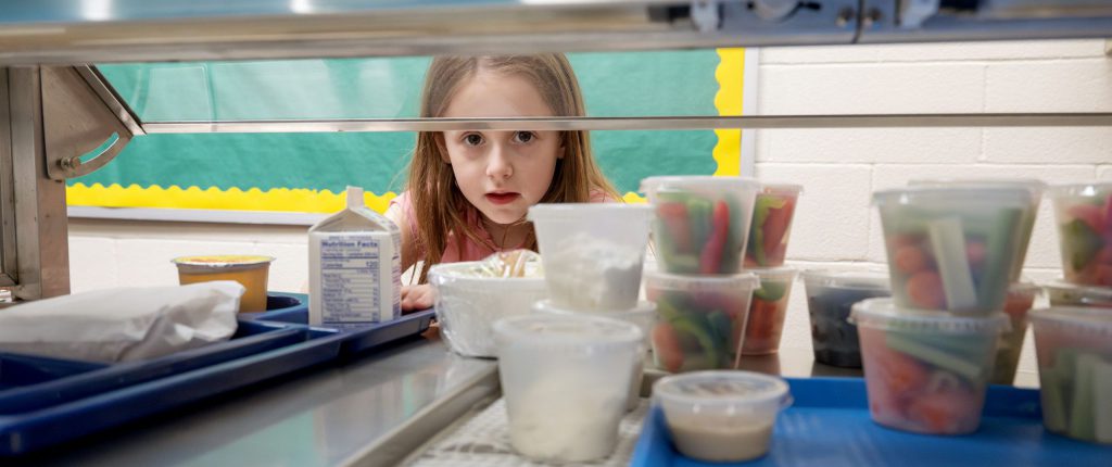 Child looking through glass in lunch line.