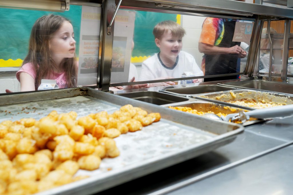 Kids with food trays happily looking through glass.